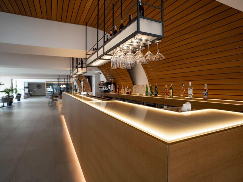 Bar dell'hotel moderno con bancone illuminato e pannelli in legno alle pareti.