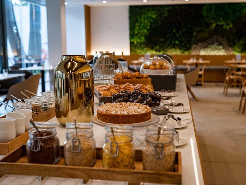Buffet con varie torte, pasticcini e bevande in un ristorante d'hotel luminoso.