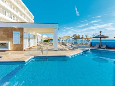Piscina dell'hotel con acqua limpida azzurra, lettini e ombrelloni sotto un cielo azzurro.