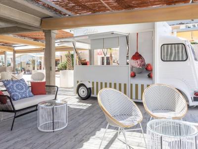 Moderner und heller Außenbereich mit weißen Rattanstühlen, Sofa und einem Retro-Eiswagen.