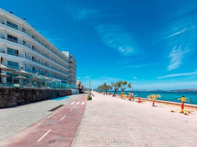 Breite Promenade mit Hotel links, blauem Himmel und Meer rechts am sonnigen Tag.