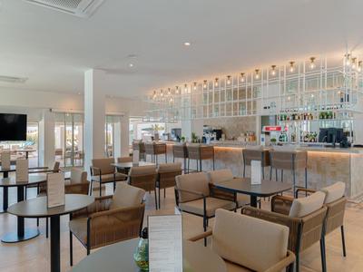 Heller, moderner Hotelbarbereich mit Holzstühlen, Tischen und beleuchtetem Tresen.