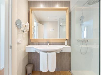 Modernes Badezimmer mit beleuchtetem Spiegel, Waschbecken, Handtüchern und Glas-Dusche.