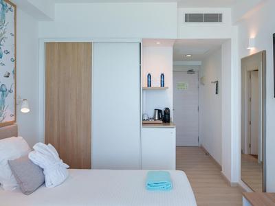 Helles Hotelzimmer mit Doppelbett, Wandkleiderschrank und Flur mit Spiegel.