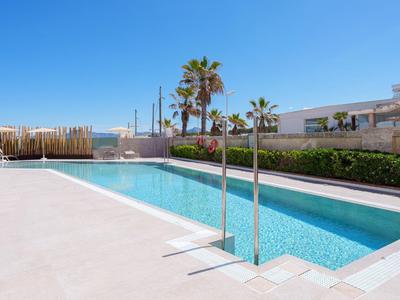 Moderner Außenpool mit klarem Wasser, Palmen und sonnigem Himmel im Hintergrund.