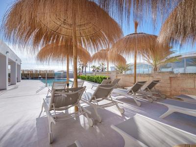 Sonnige Hotelterrasse mit Liegestühlen und Strohm Sonnenschirmen am Poolbereich.