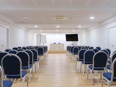 Konferenzraum mit Stuhlreihen, Tischen, Flipchart und Fernseher an der Wand.