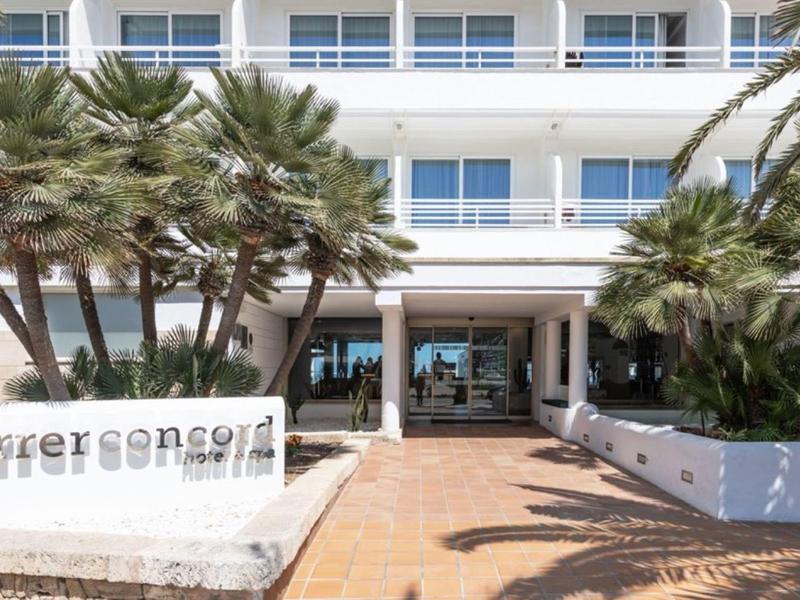 Moderner Hotel-Eingang mit weißen Fassaden, Palmen und Glasfront unter blauem Himmel.