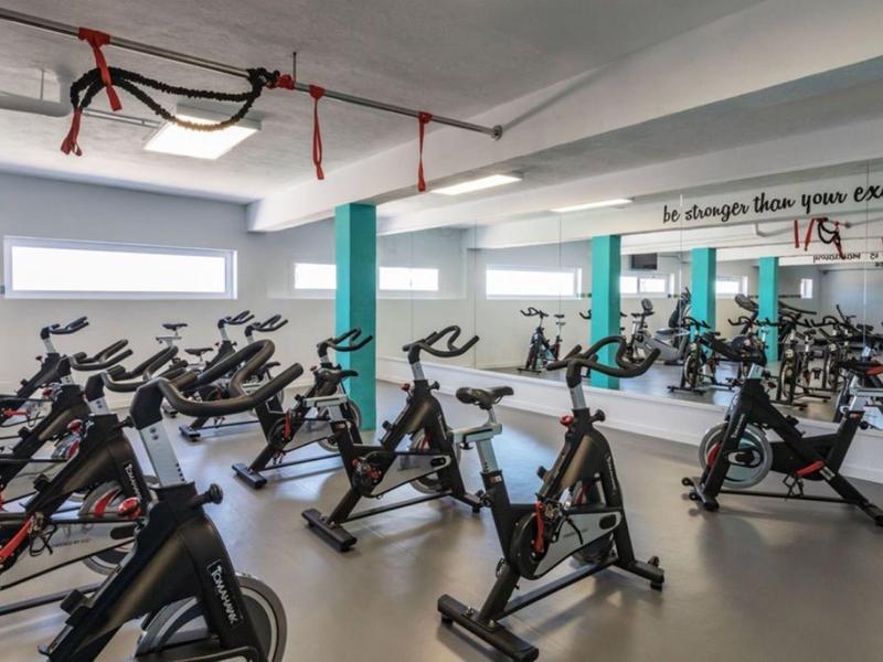 Innenraum eines Fitnessstudios mit vielen schwarzen Spinning-Rädern auf grauem Boden und Spiegelwand.