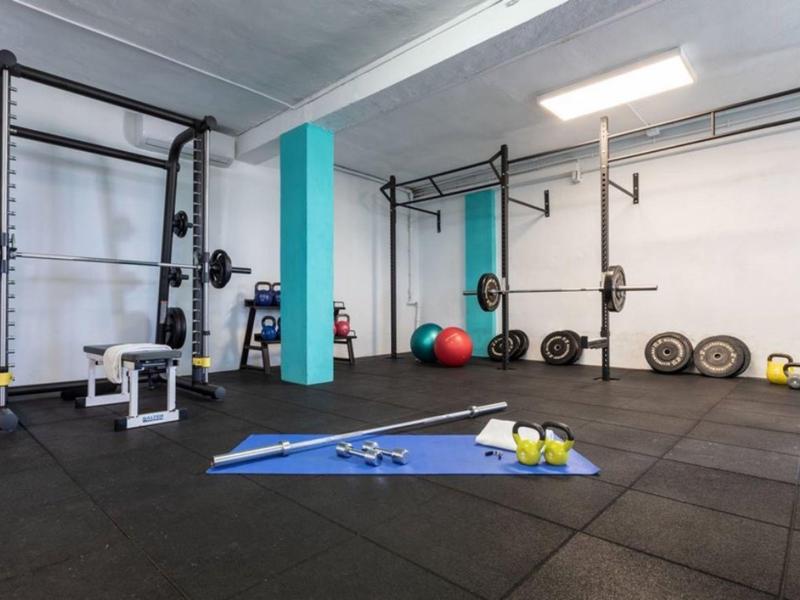 Moderner Fitnessraum mit Kraftstation, Gymnastikmatte, Hanteln, Bällen und Kettlebells auf schwarzem Boden.