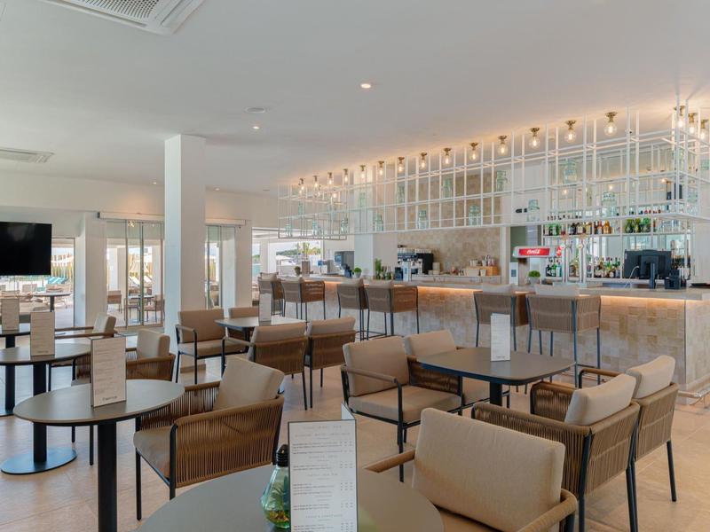 Heller, moderner Hotelbarbereich mit Holzstühlen, Tischen und beleuchtetem Tresen.