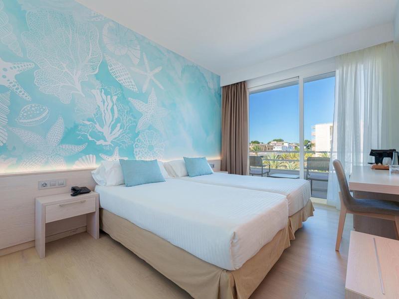 Helles Hotelzimmer mit Doppelbett, blauer Wanddekoration und Balkon mit Aussicht.