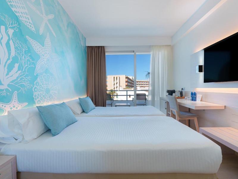 Modernes Hotelzimmer mit zwei Betten, großem Fenster und Balkon mit Stadtblick.