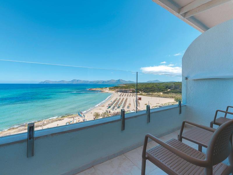 Balkon mit zwei Stühlen und Blick auf einen Sandstrand und das Meer bei klarem Himmel.