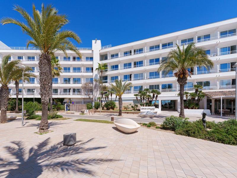 Modernes Hotel mit Palmen und Sonnenterrasse unter klarem blauem Himmel.