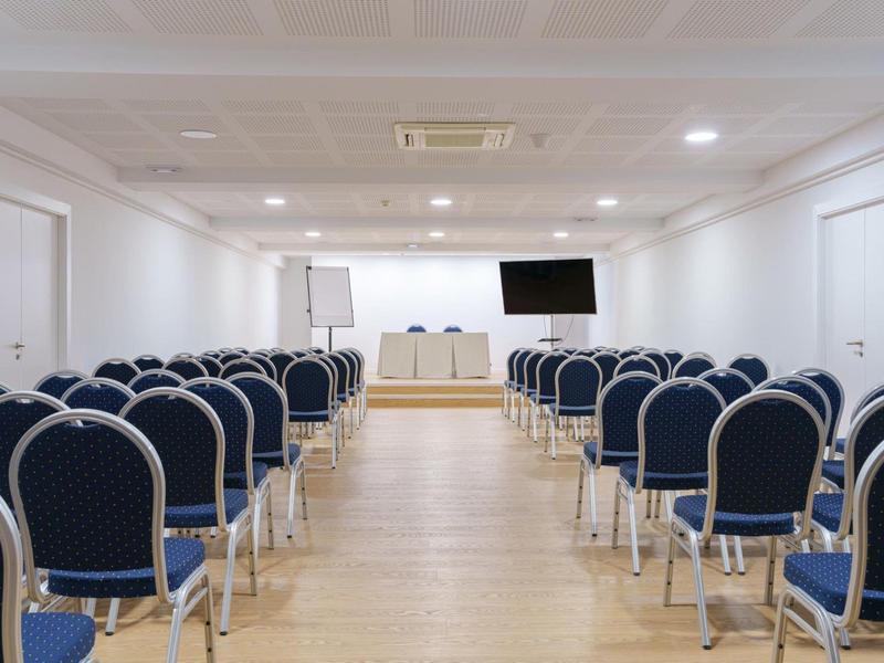 Konferenzraum mit Stuhlreihen, Tischen, Flipchart und Fernseher an der Wand.