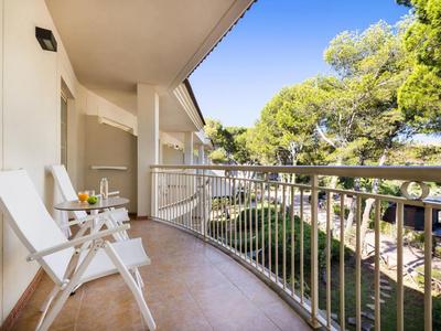 Balcon avec deux chaises blanches et table avec vue sur des arbres verts et un ciel bleu.