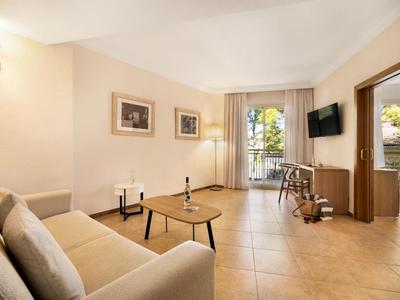 Salon lumineux avec canapé, tables et vue sur balcon dans une chambre d'hôtel.