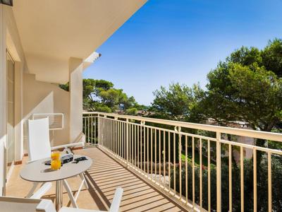 Balcon avec chaises et table, vue sur des arbres et ciel bleu.