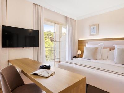 Chambre d'hôtel lumineuse avec lit double, bureau et balcon avec vue.