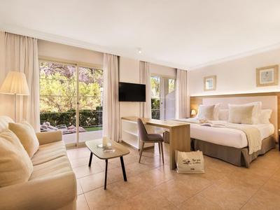 Lichte hotelkamer met tweepersoonsbed, bank, tafel, stoelen en uitzicht op tuin.