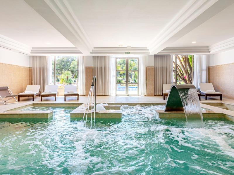 Piscine intérieure lumineuse avec sièges et cascade dans un espace bien-être.