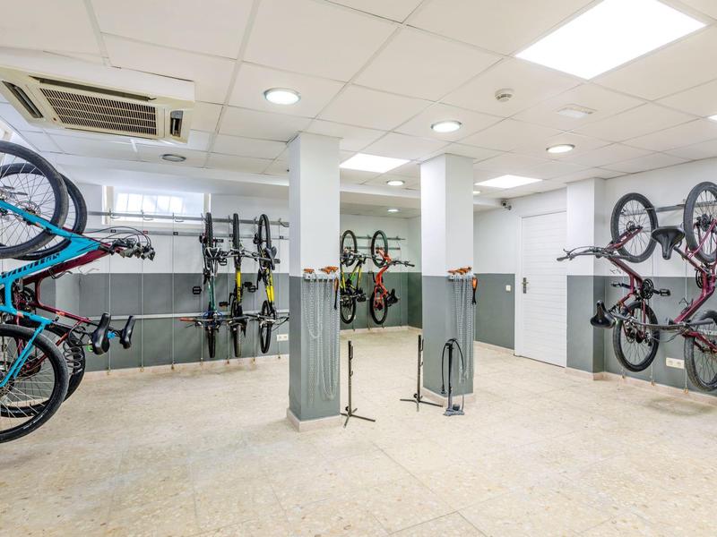 Salle de vélos lumineuse avec plusieurs vélos accrochés aux murs et des ateliers de réparation au centre.