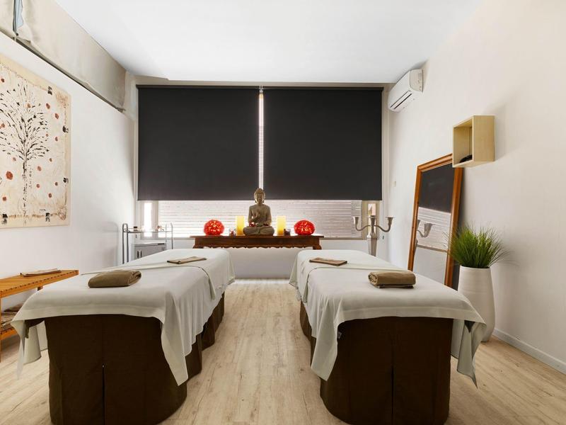 Salle de thérapie calme avec deux tables de massage et décoration à la fenêtre.