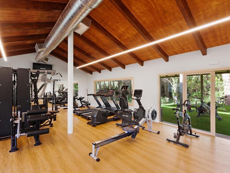 Salle de sport moderne avec sol en bois, plafond à poutres en bois et vue sur le jardin.