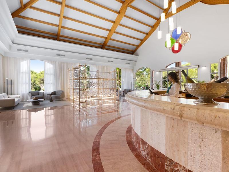 Hall d'hôtel élégant avec plafond blanc, comptoir d'accueil incurvé et lumière naturelle abondante.