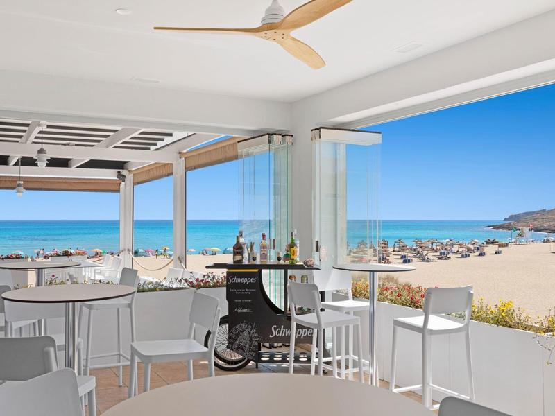 Espace repas intérieur ouvert avec vue sur la plage et la mer.