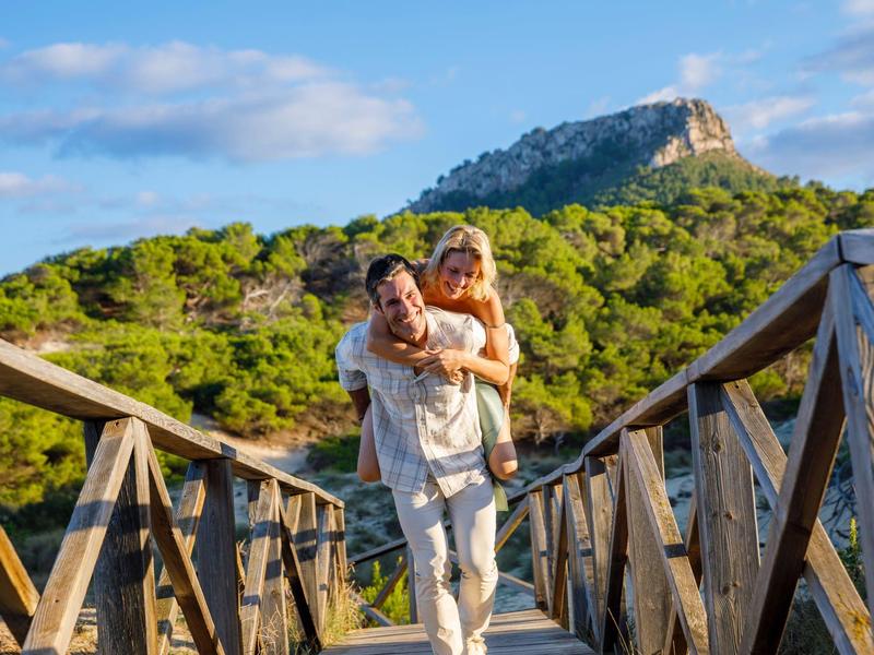 Couple heureux sur un pont en bois avec montagne boisée en arrière-plan.