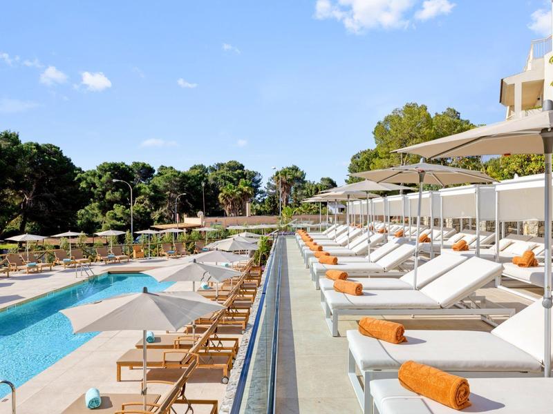 Espace piscine d'hôtel moderne avec chaises longues et parasols sous un ciel bleu.