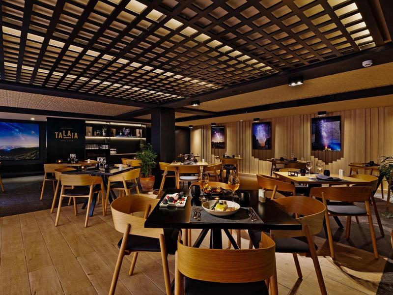 Restaurant élégant avec éclairage chaleureux, mobilier en bois et plafond moderne.