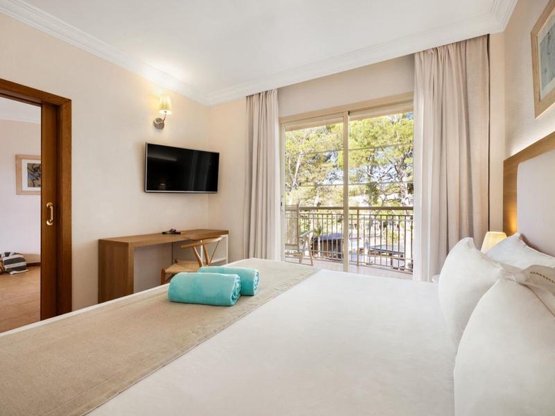 Chambre d'hôtel confortable avec lit, télévision et balcon donnant sur les arbres.