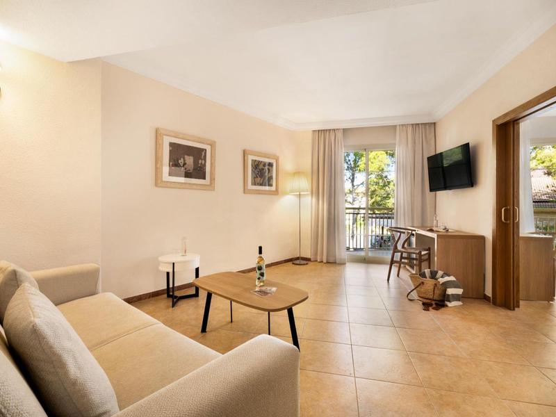 Salon lumineux avec canapé, tables et vue sur balcon dans une chambre d'hôtel.