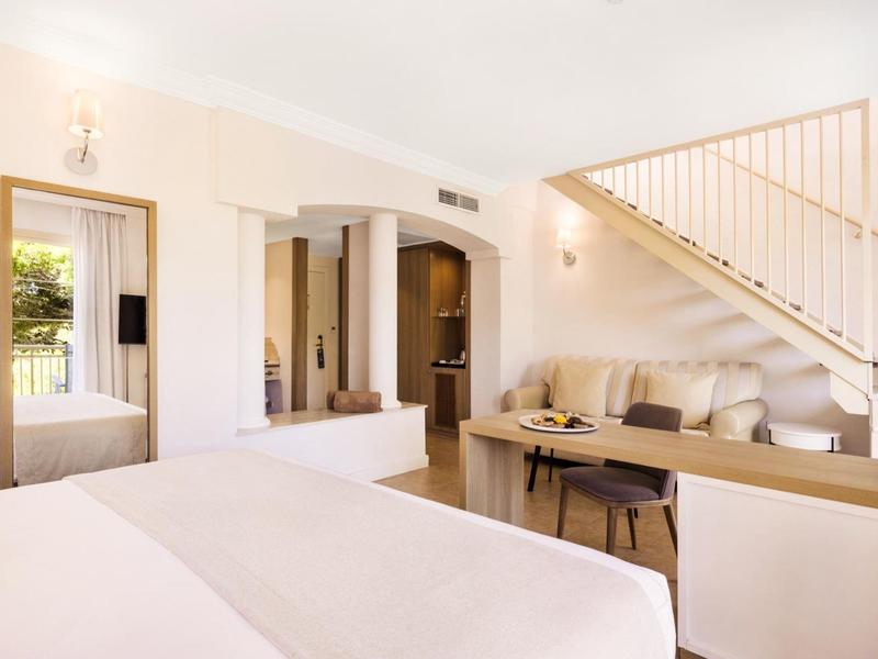 Chambre d'hôtel lumineuse et moderne avec lit, coin salon et escalier.