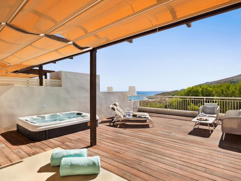Grande terrasse en bois avec jacuzzi, chaises longues et vue superbe sur la mer et les collines.