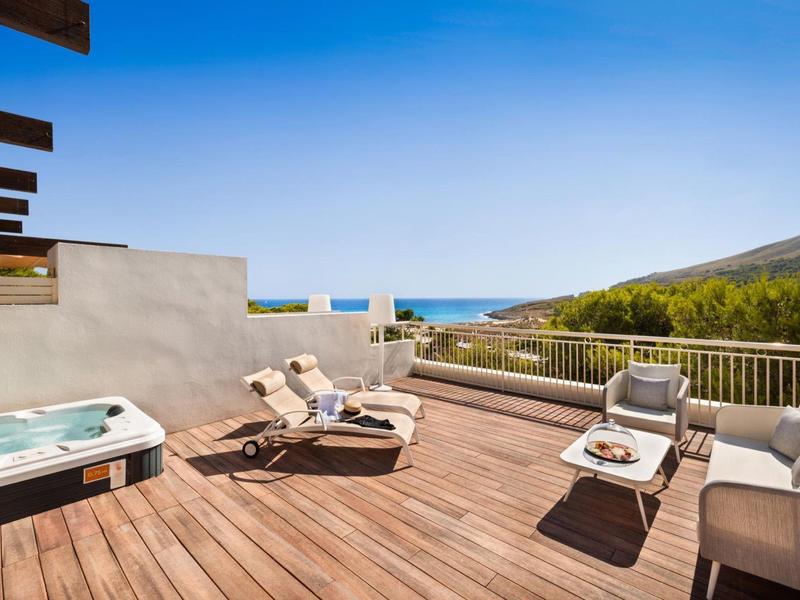 Grande terrasse avec sol en bois, chaises longues, jacuzzi et vue sur la mer.