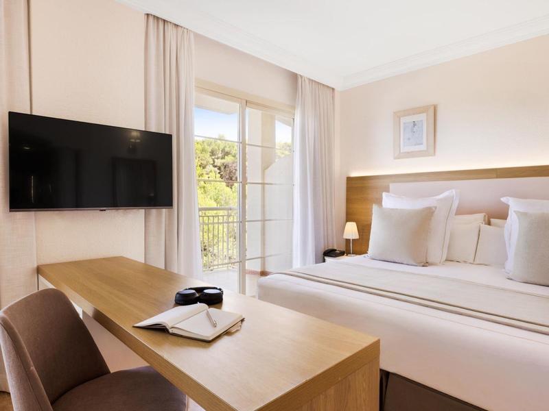 Chambre d'hôtel lumineuse avec lit double, bureau et balcon avec vue.