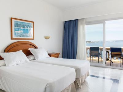 Hotel room with two single beds, balcony, and sea view.