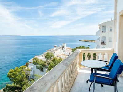 Balcony with blue cushioned chairs and table overlooking the sea under clear sky.