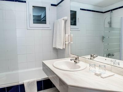 Bright bathroom with sink, mirror, bathtub, and white towels hanging on the wall.