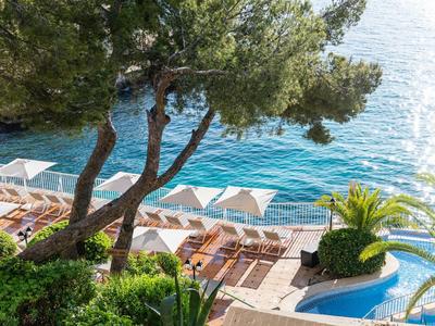 View of sun loungers and umbrellas on a coast with clear blue water and trees.