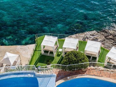 View of a pool area by the sea with white cabanas and clear blue water.