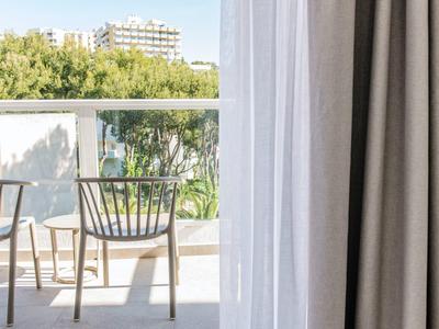 Two wooden chairs and a small table on a sunny balcony overlooking trees and buildings.