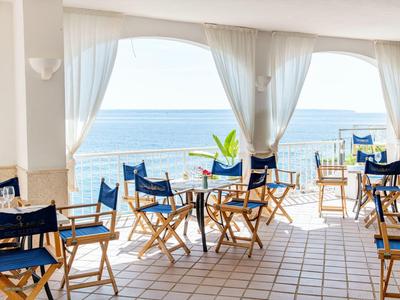 Open dining area with sea view, wooden tables and blue folding chairs on tiled floor.