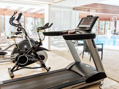 Modern fitness equipment like treadmill and exercise bike in a bright gym with pool view.