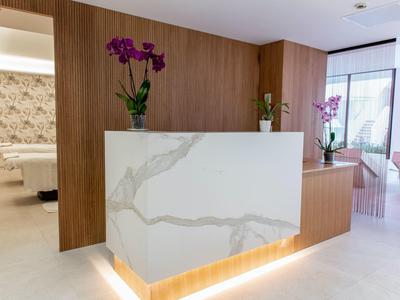 Modern reception area with white marble counter and wood paneling, decorated with orchids.