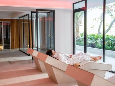Person relaxing on modern lounge chair in bright room with large glass windows.